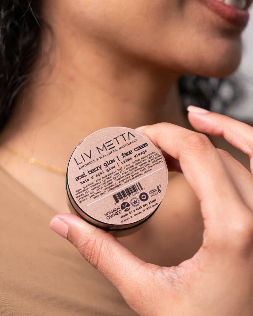 A person holding a container of Acai Berry Glow Face Cream by LIV METTA.