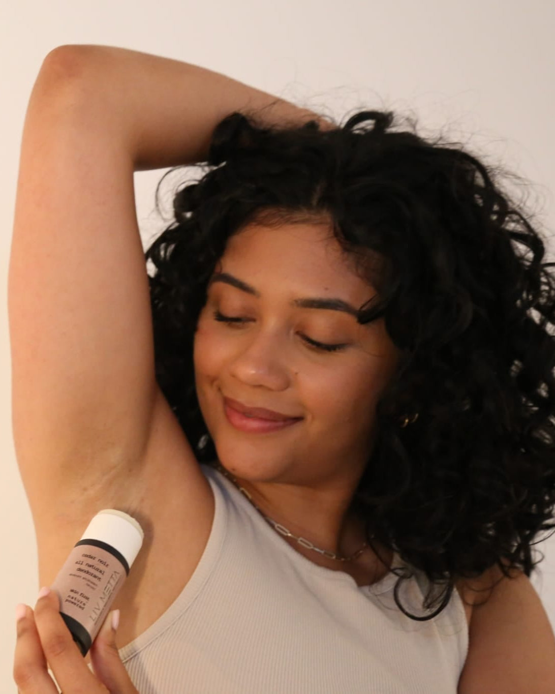 Woman applying deodorant to her armpit against a plain background