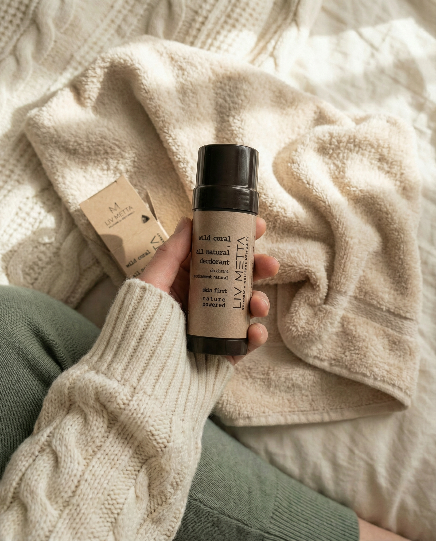 Hand holding a bottle of LIV MECCA product with a textured beige blanket in the background