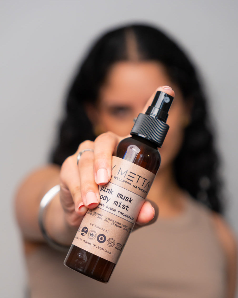 A person holding a bottle of Pink Musk Body Mist with a spray nozzle. The label includes the product name and the brand, Metta.