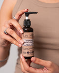 A person holding a bottle of Grapefruit Facial Cleansing Oil with a pump dispenser. The label includes the brand name 'LIV META' and the product name 'grapefruit glow facial cleansing oil'.