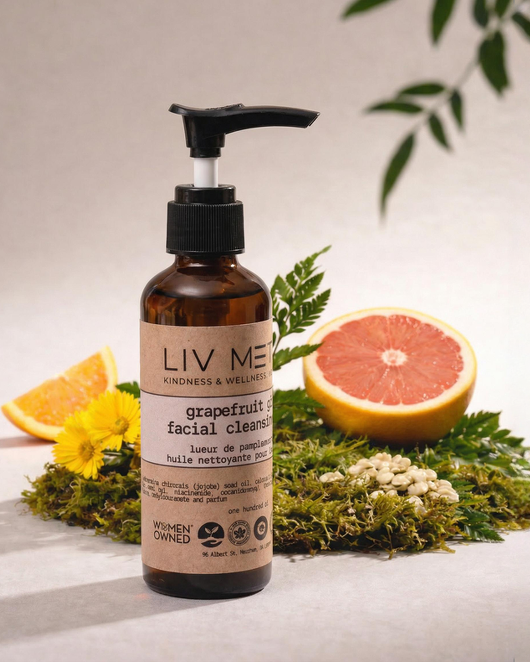 Bottle of LIV MEtta skincare product with grapefruit slices and greenery on a neutral background