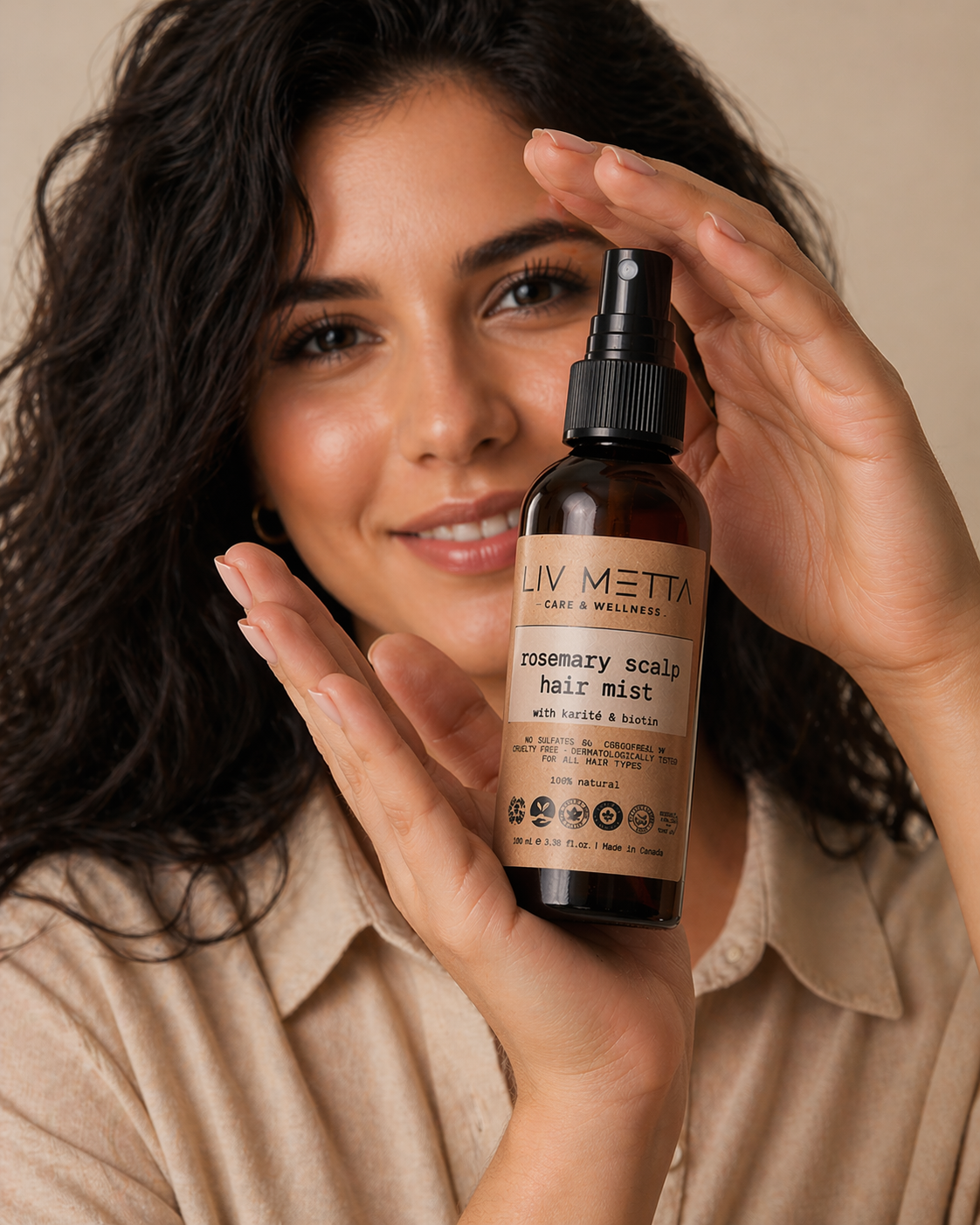 Woman holding a bottle of 'Livmetta' rosemary scalp hair mist against a beige background
