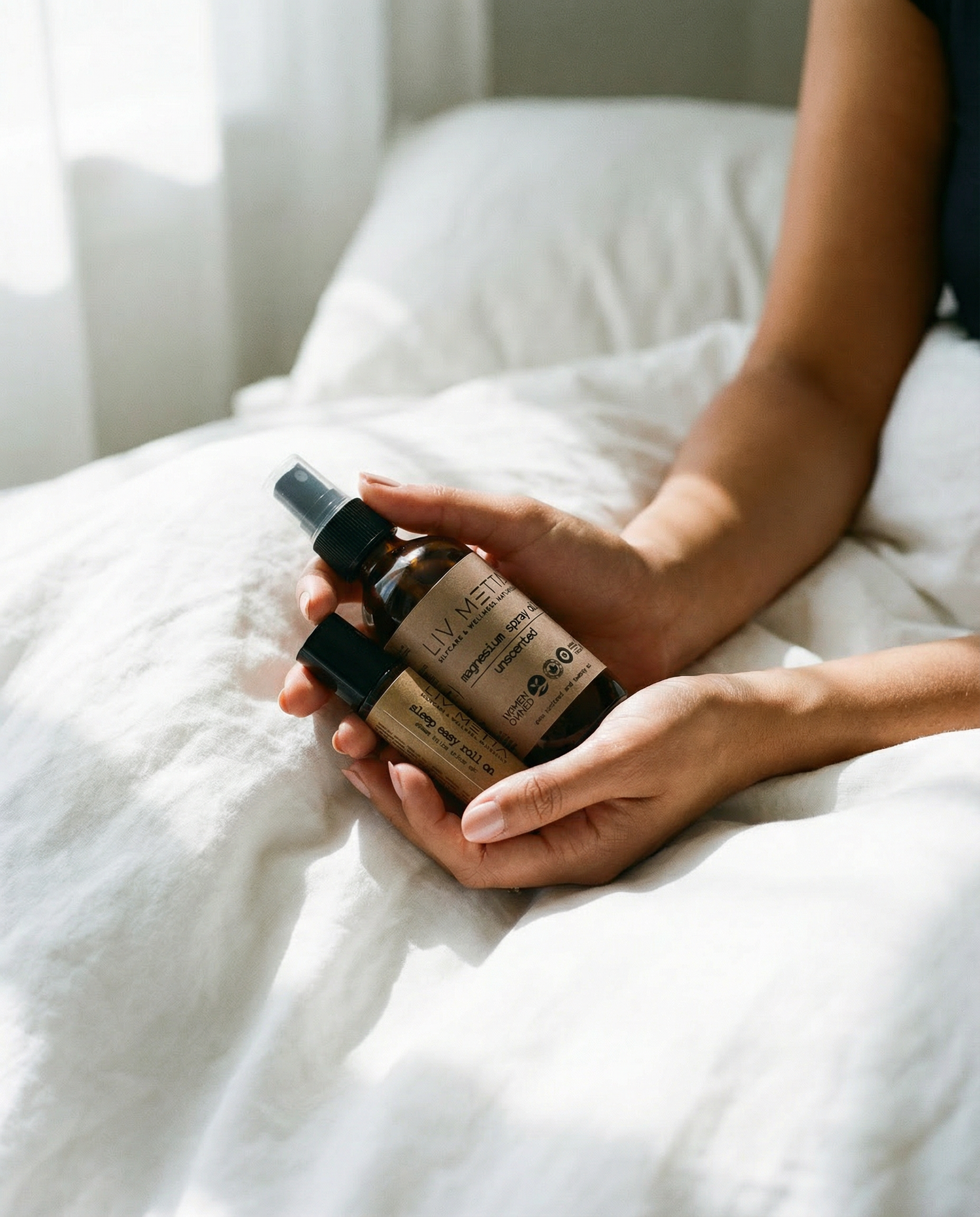 Person holding skincare bottles on a white blanket