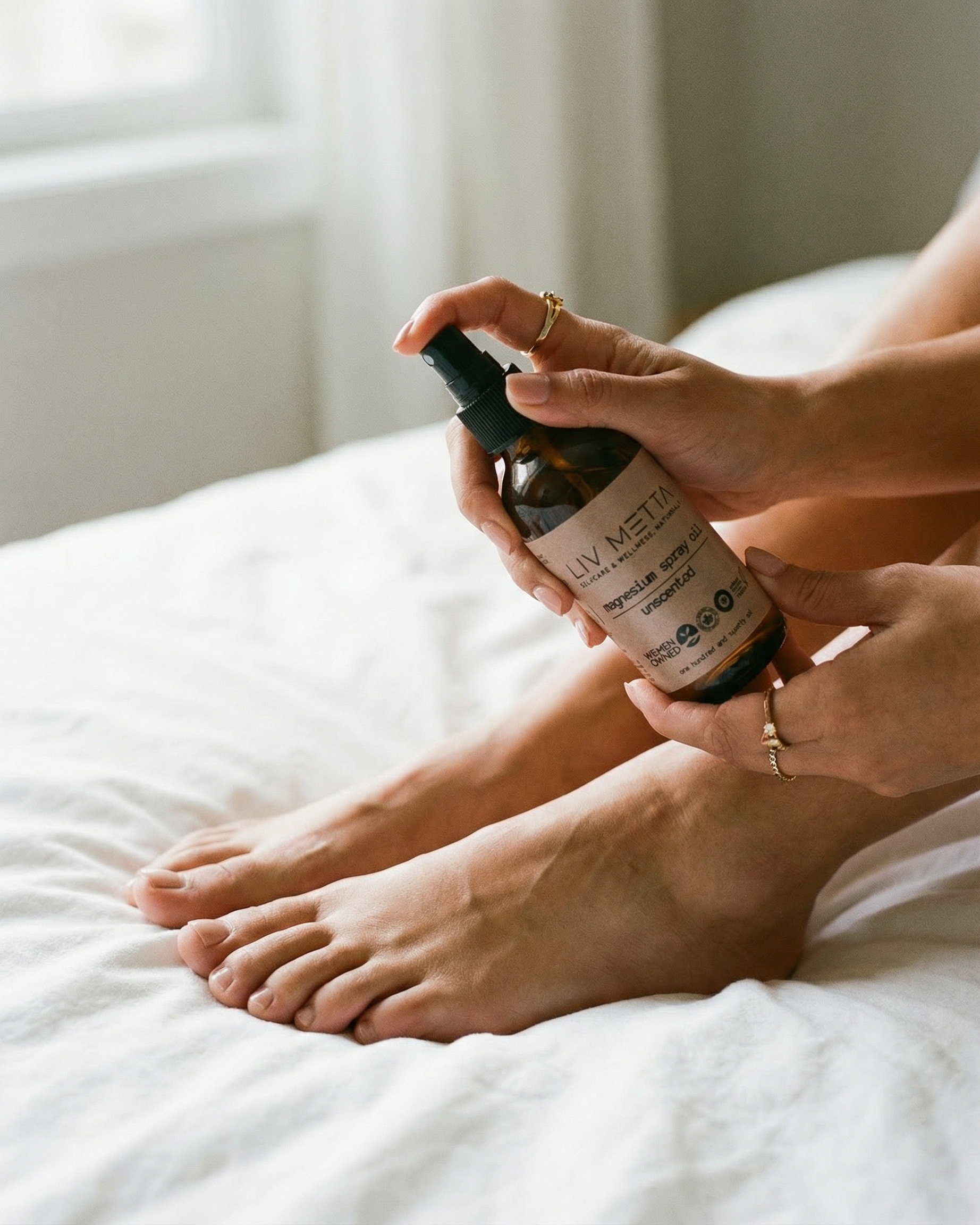 Person applying a spray from a bottle labeled Mg Spray Oil o their foot on a bed.
