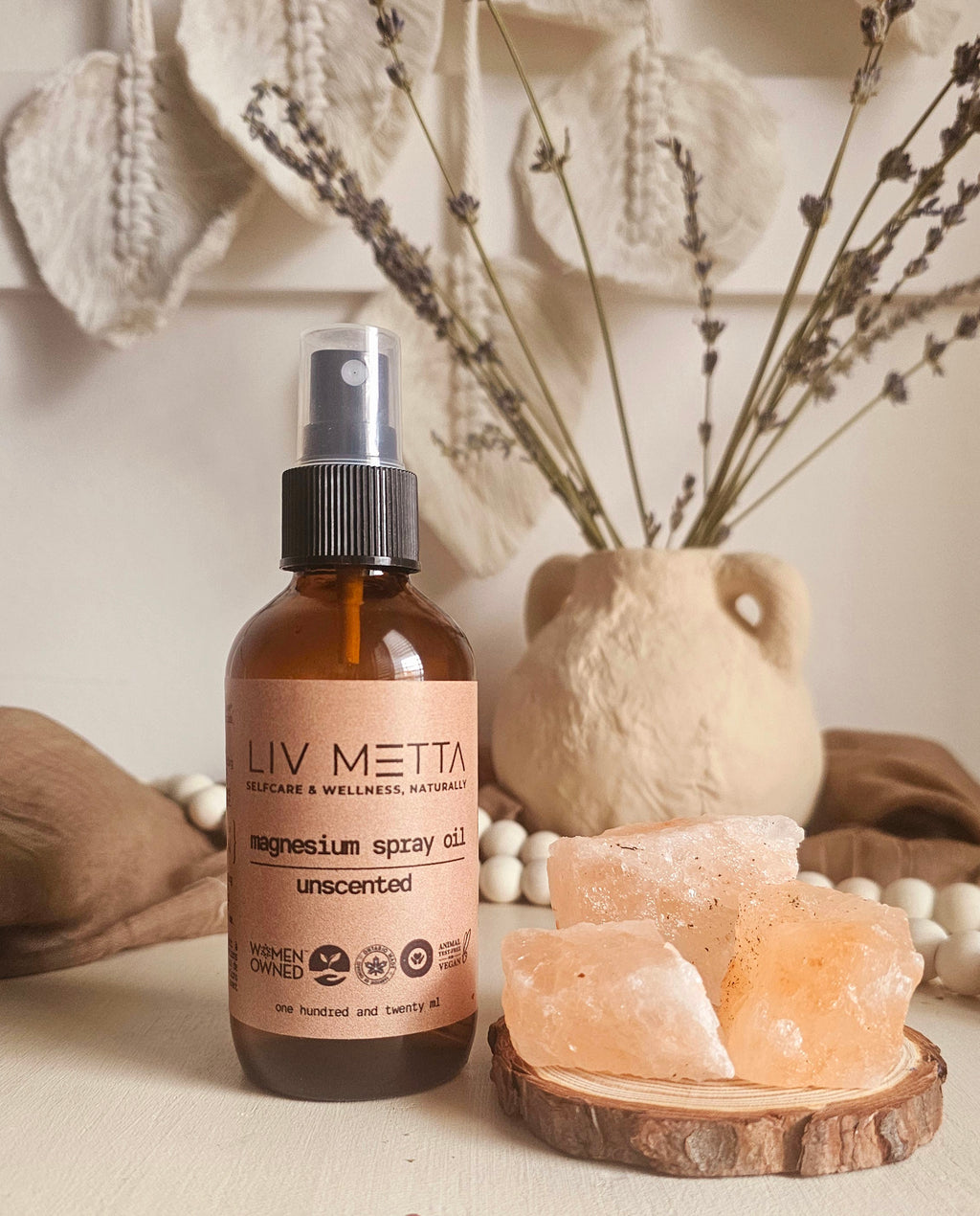 A bottle of Topical Magnesium Oil Spray by LIV. METTA, unscented, displayed on a wooden surface with decorative items in the background.