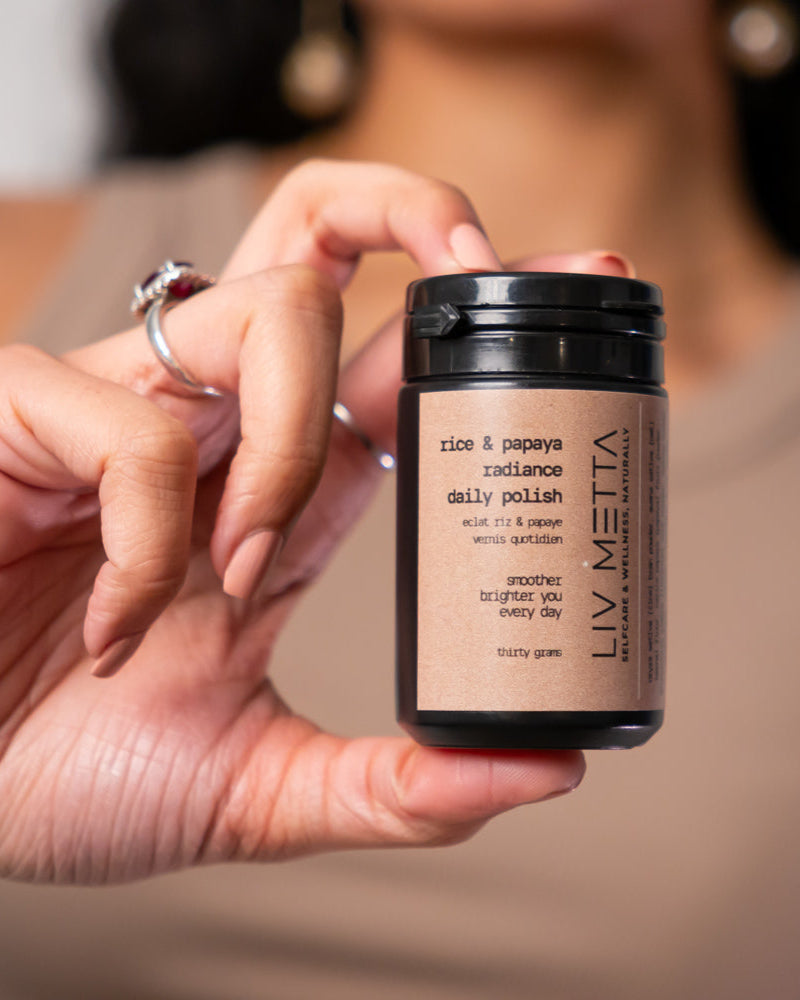 A person holding a container of Rice & Papaya Radiance Daily Polish, a skin care product.