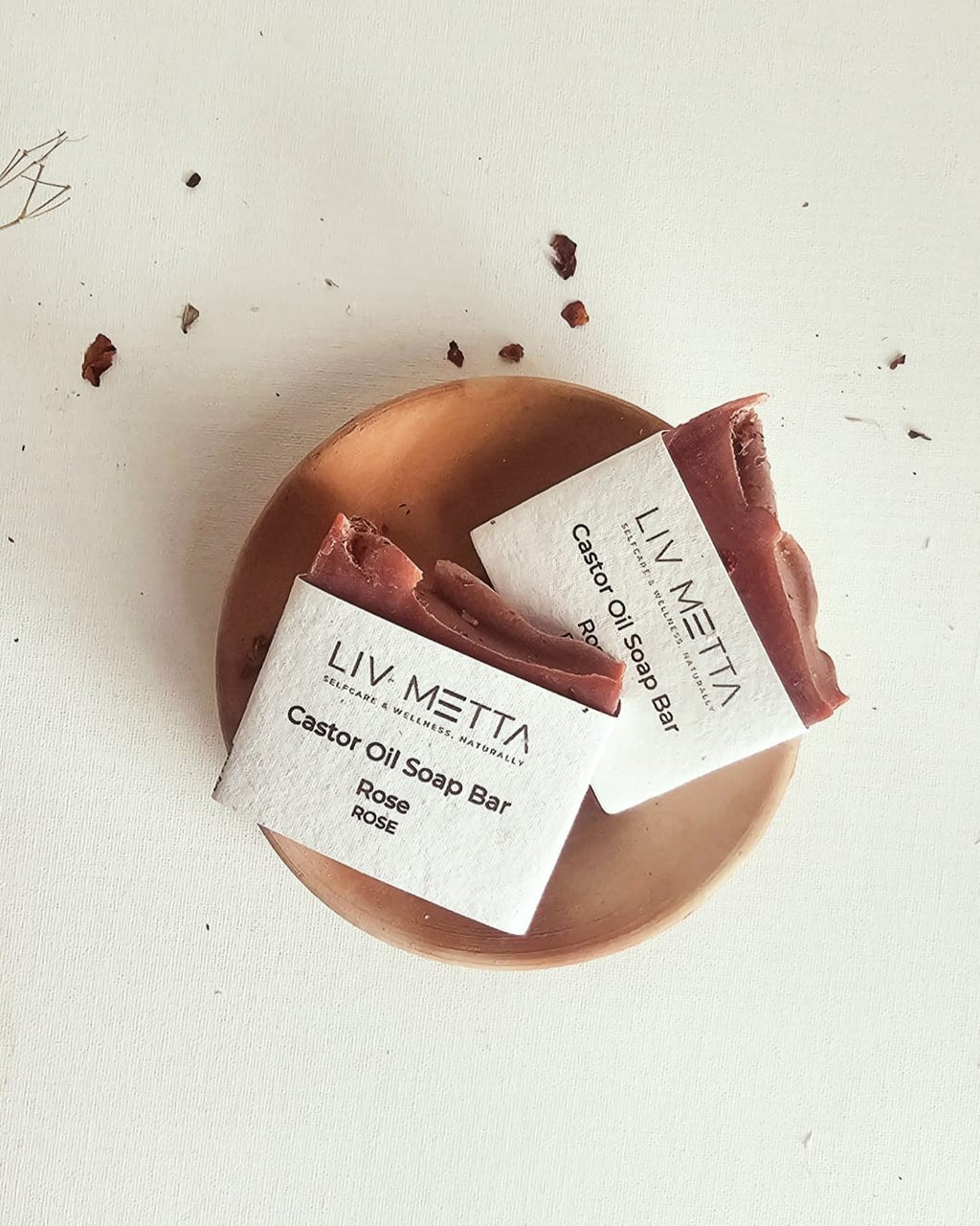 A soap bar with a pink label on a wooden surface, with the brand name 'Liv Metta' and 'Castor Oil Soap Bar' written on it.