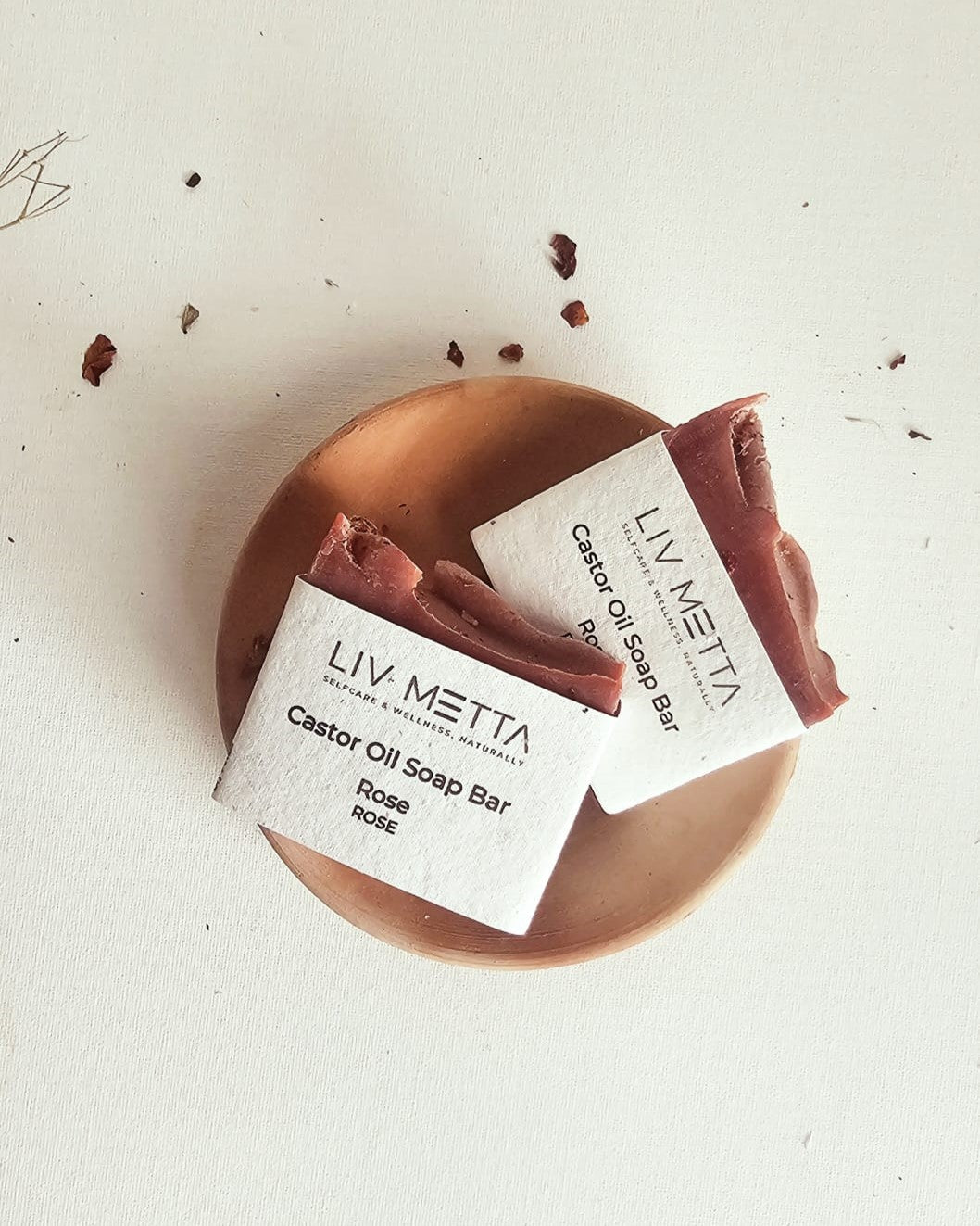 A soap bar with a pink label on a wooden surface, with the brand name 'Liv Metta' and 'Castor Oil Soap Bar' written on it.