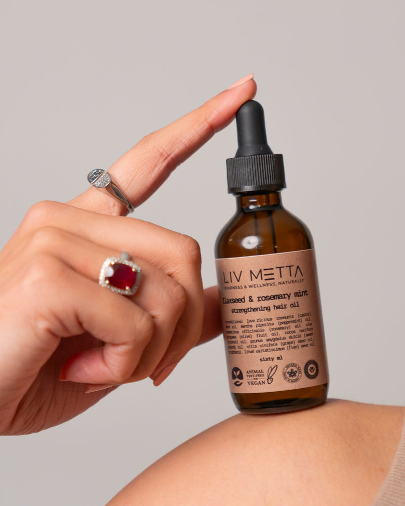 A person's hand holding a bottle of Flaxseed & Rosemary Mint Hair Oil with the brand name visible on the label.