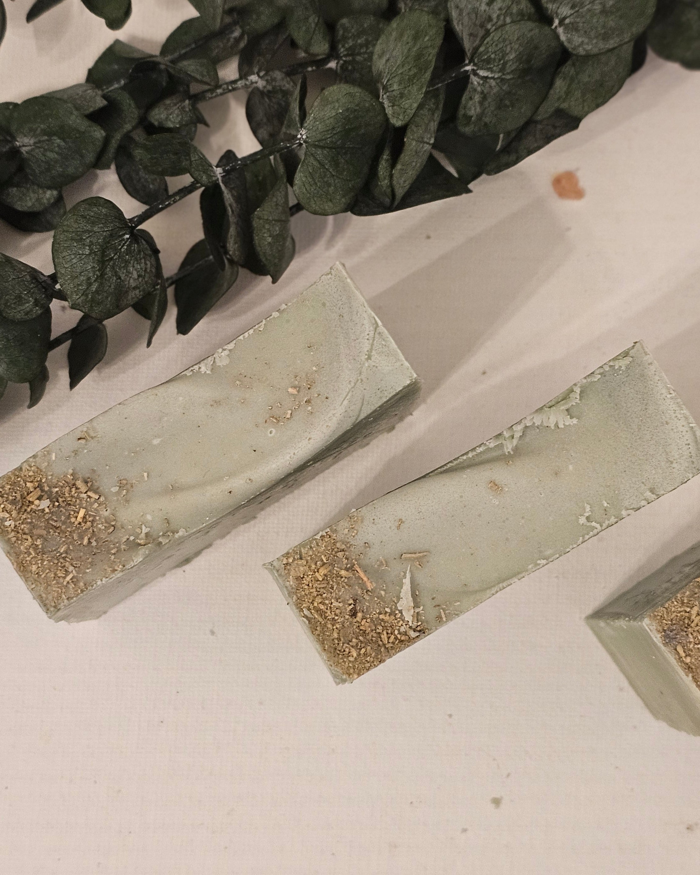 Handmade rectangular soap bars with a greenish tint and gold flecks, displayed alongside green leaves.