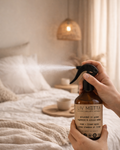 Person holding a 'LIV METTA' spray bottle in a cozy bedroom setting.