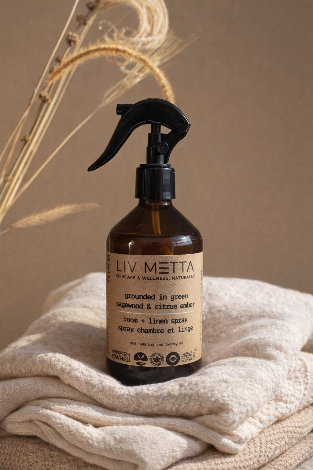Brown spray bottle with a label on a beige surface Liv Metta Room Spray