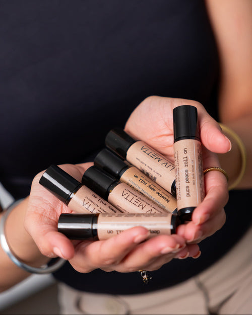 A person holding several roll-on bottles with black caps, likely containing therapeutic-grade essential oils for aromatherapy.