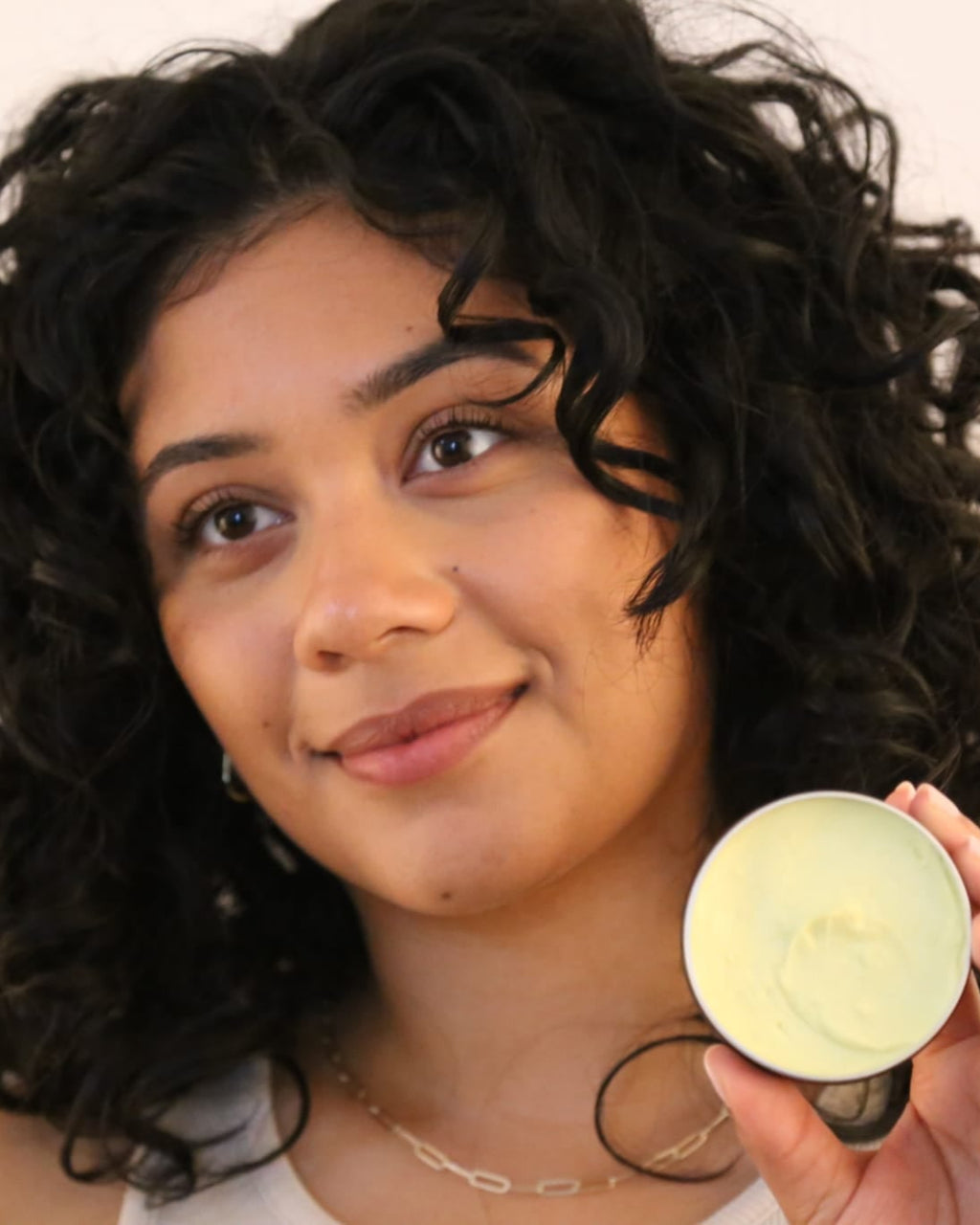 Woman holding a small round container with a greenish substance.