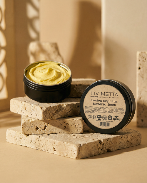 Jar of yellow body butter with black lid on stone surface, 'LIV METTA' branding visible.