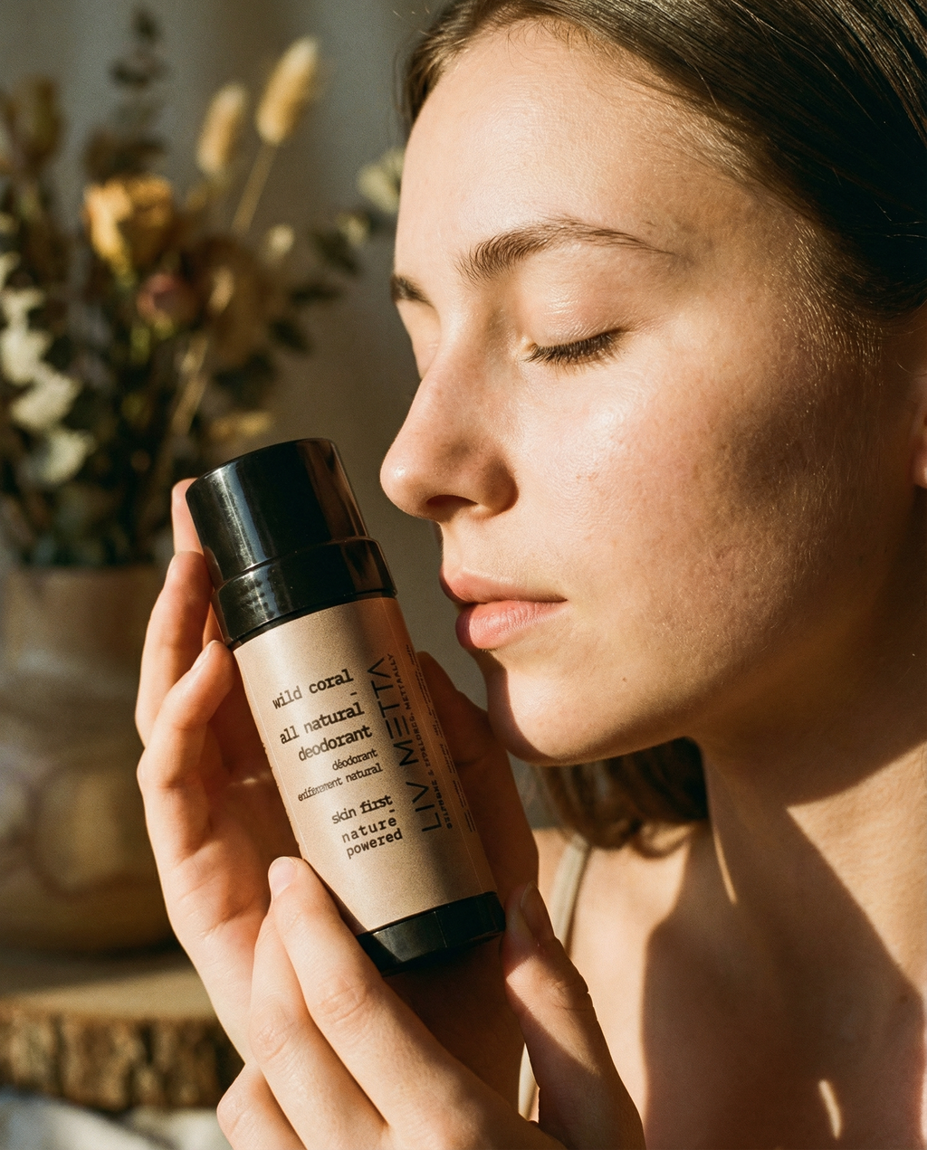 Woman holding a bottle of Lavretta solid coral all natural deodorant with a blurred background