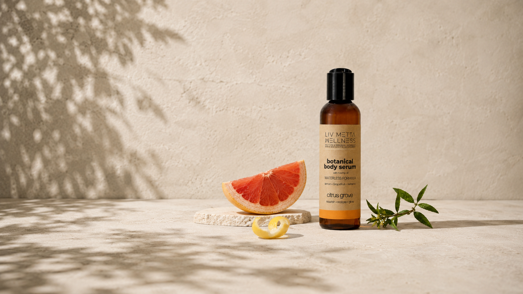 A bottle of Lav Muta Relaxing Body Serum stands on a light stone surface beside a grapefruit slice, a lemon wedge, and green sprigs, against a textured beige wall with leaf shadows.